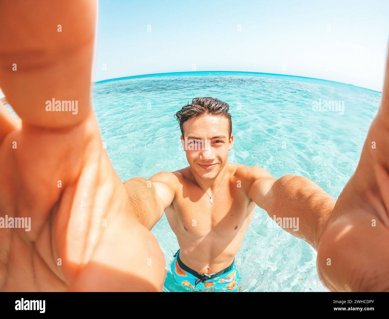 Portrait d'un jeune homme heureux prenant un selfie de lui sur la plage dans une eau turquoise bleue ayant du plaisir et appréciant seul des vacances à l'extérieur. Banque D'Images