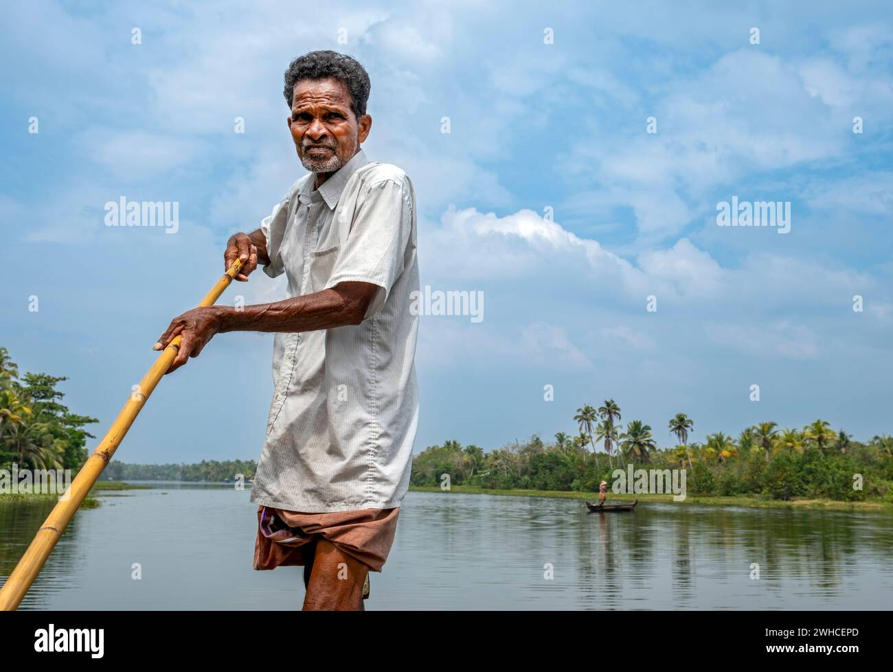 Un homme navigue un bateau à travers les canaux des backwaters du Kerala en utilisant un long poteau, le lac Vembanad, Kerala, Inde Banque D'Images