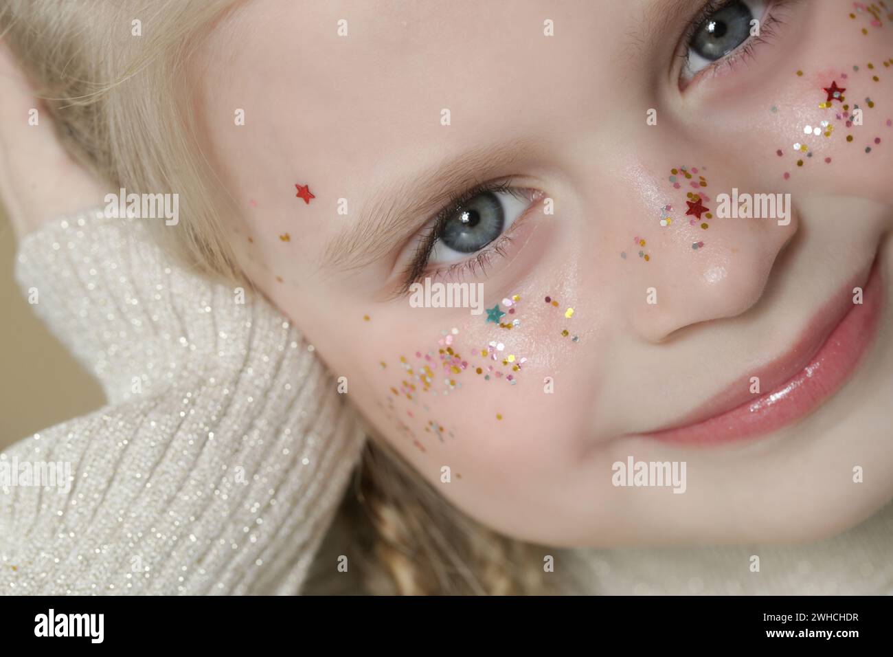 Portrait de petite fille blonde mignonne avec des yeux bleus et des paillettes sur son visage. Banque D'Images