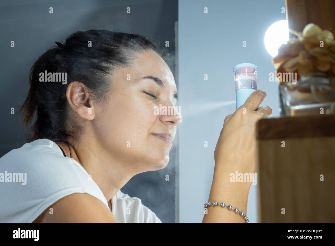 Femme utilisant un vaporisateur facial dans sa routine quotidienne de beauté faciale. Soins quotidiens de la peau, hydratation et dermatologie. Vaporisateur domestique. Banque D'Images