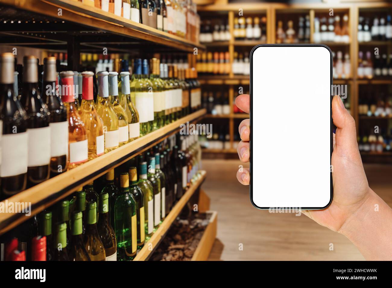 Téléphone intelligent avec écran vide dans la main de la femme devant le magasin d'alcool. Commande et achat en ligne de boissons alcoolisées. Maquette pour l'application mobile. Banque D'Images