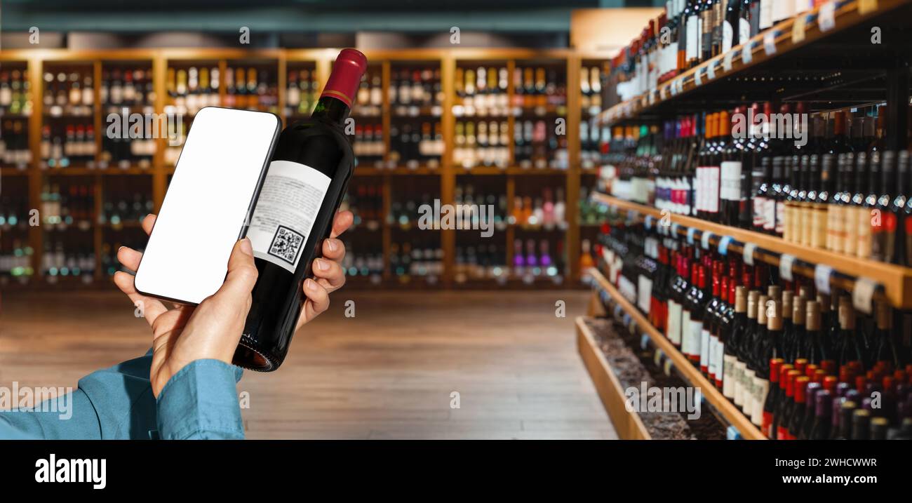 Personne utilisant le téléphone intelligent pour scanner e-étiquette sur la bouteille de vin dans le magasin d'alcool. Banque D'Images
