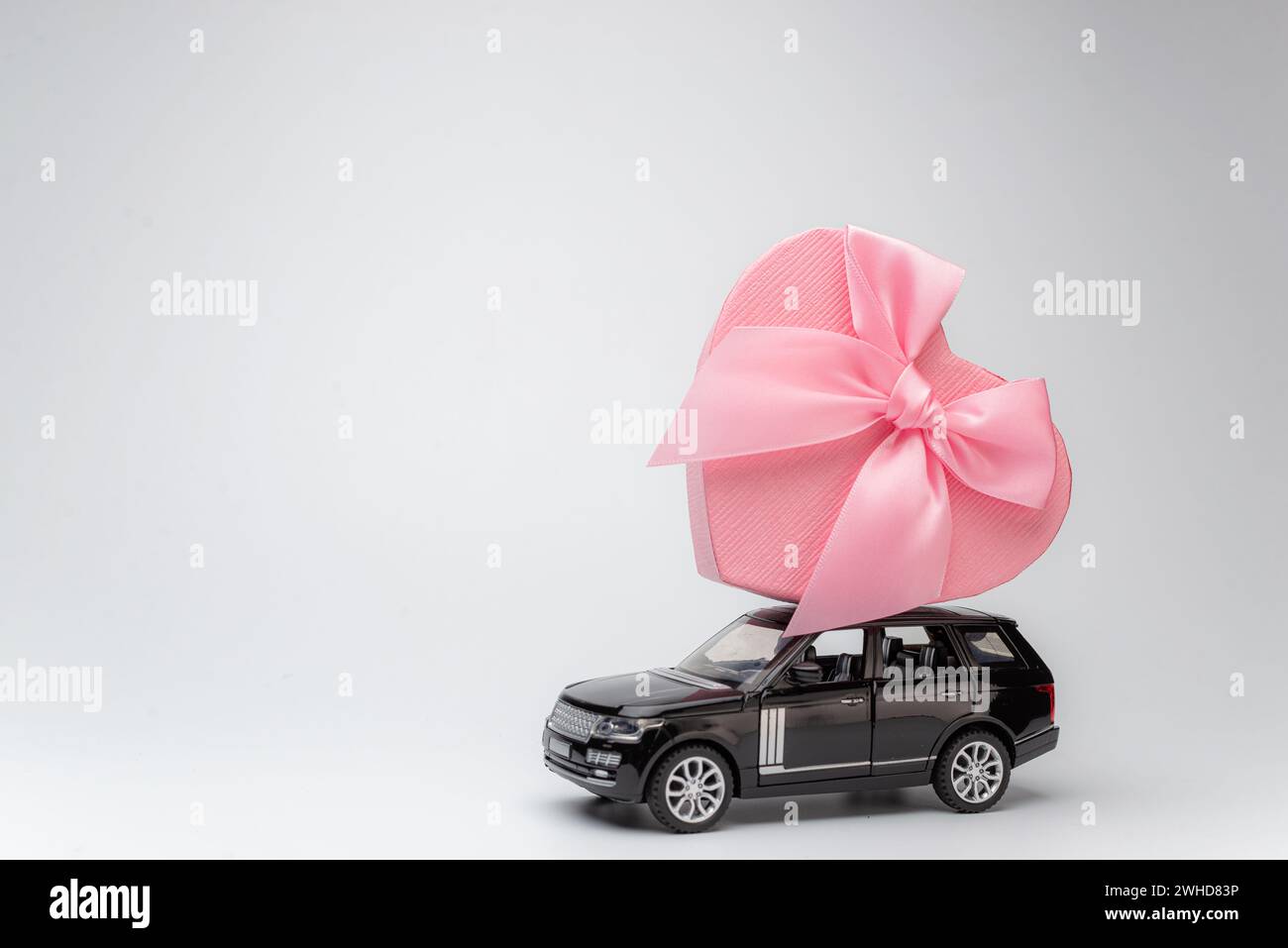 voiture avec une boîte cadeau sur le toit sur fond rose. Bonne Saint Valentin, fête des mères, 8 mars, concept de carte de vacances de la Journée mondiale de la femme, fleur Banque D'Images