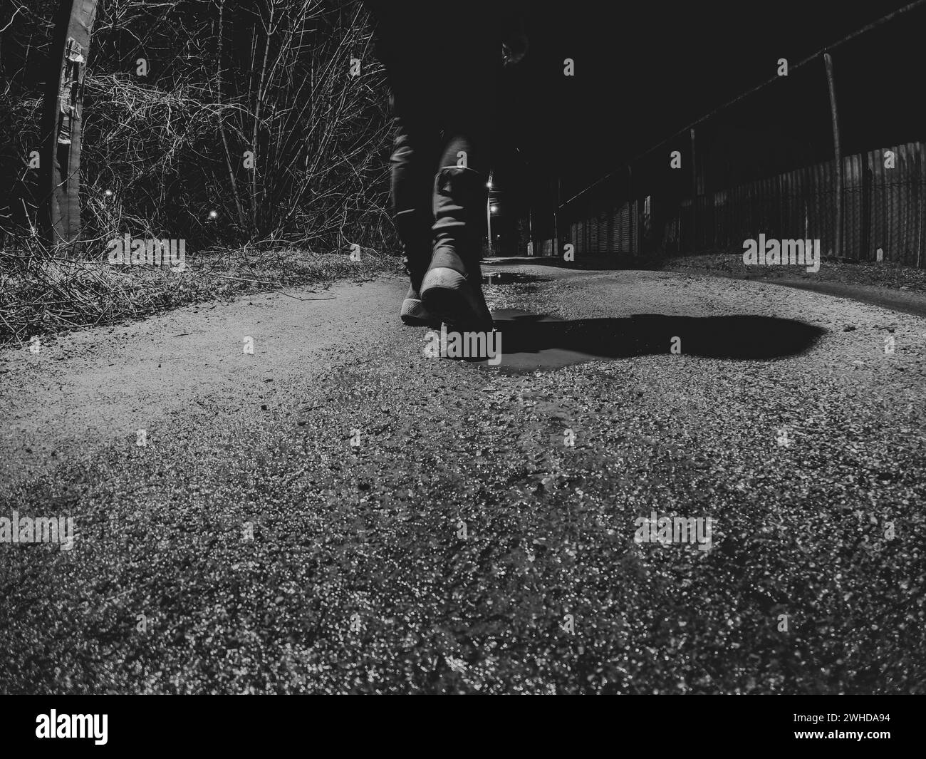 Une fille marche le long d'une route humide d'hiver à la maison dans l'obscurité, vue de bas en haut, photo noir et blanc, pieds sur la route dans l'obscurité Banque D'Images