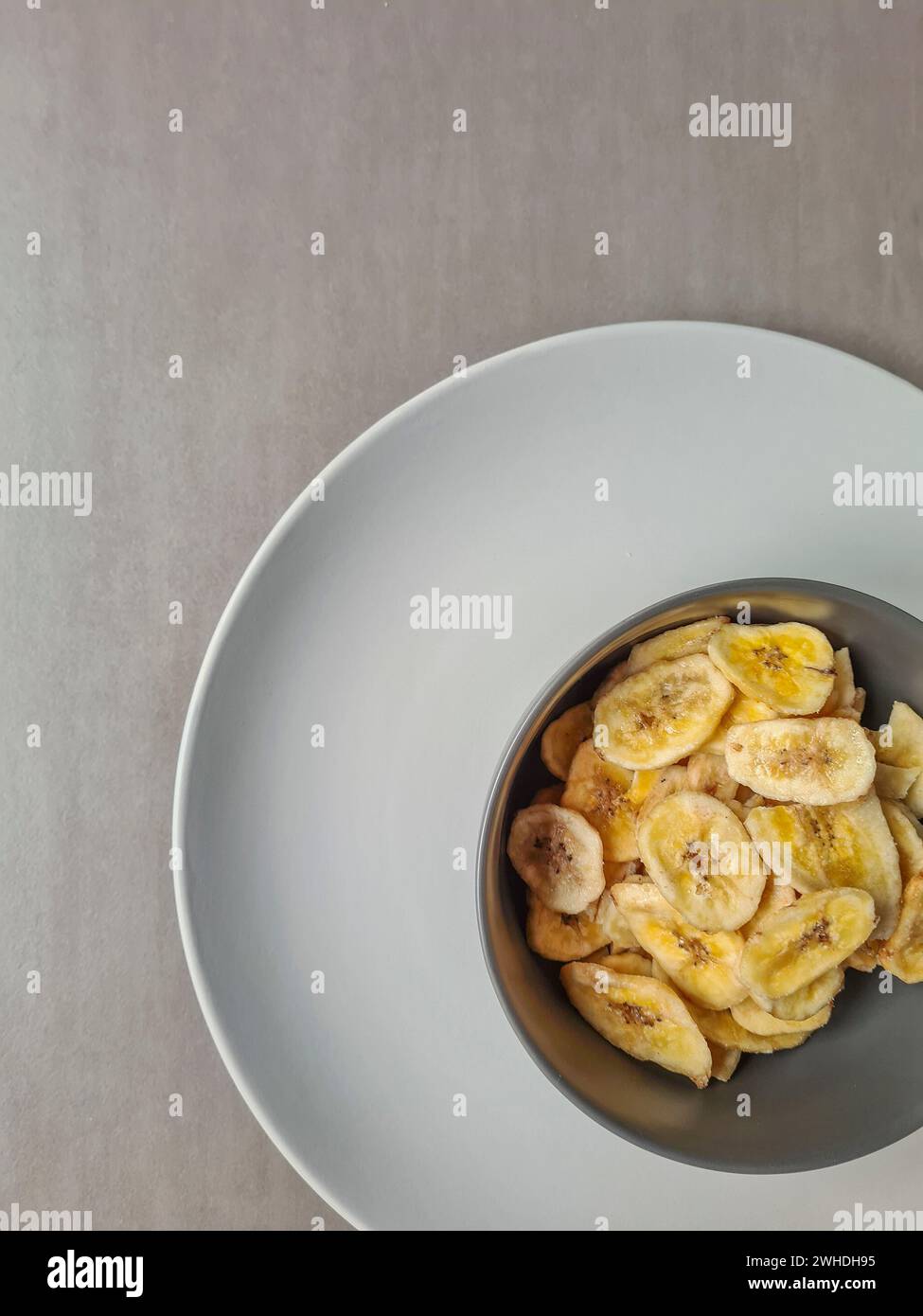 Chips de banane dans un bol gris sur une assiette gris clair comme dessert et collation entre les repas Banque D'Images