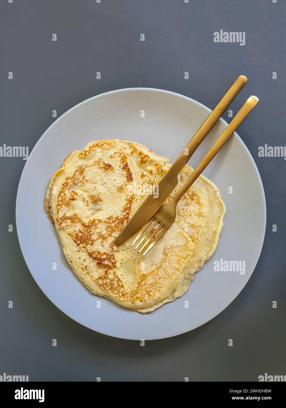 Crêpes sur une assiette grise avec des couverts dorés, un couteau et une fourchette sur un fond gris Banque D'Images