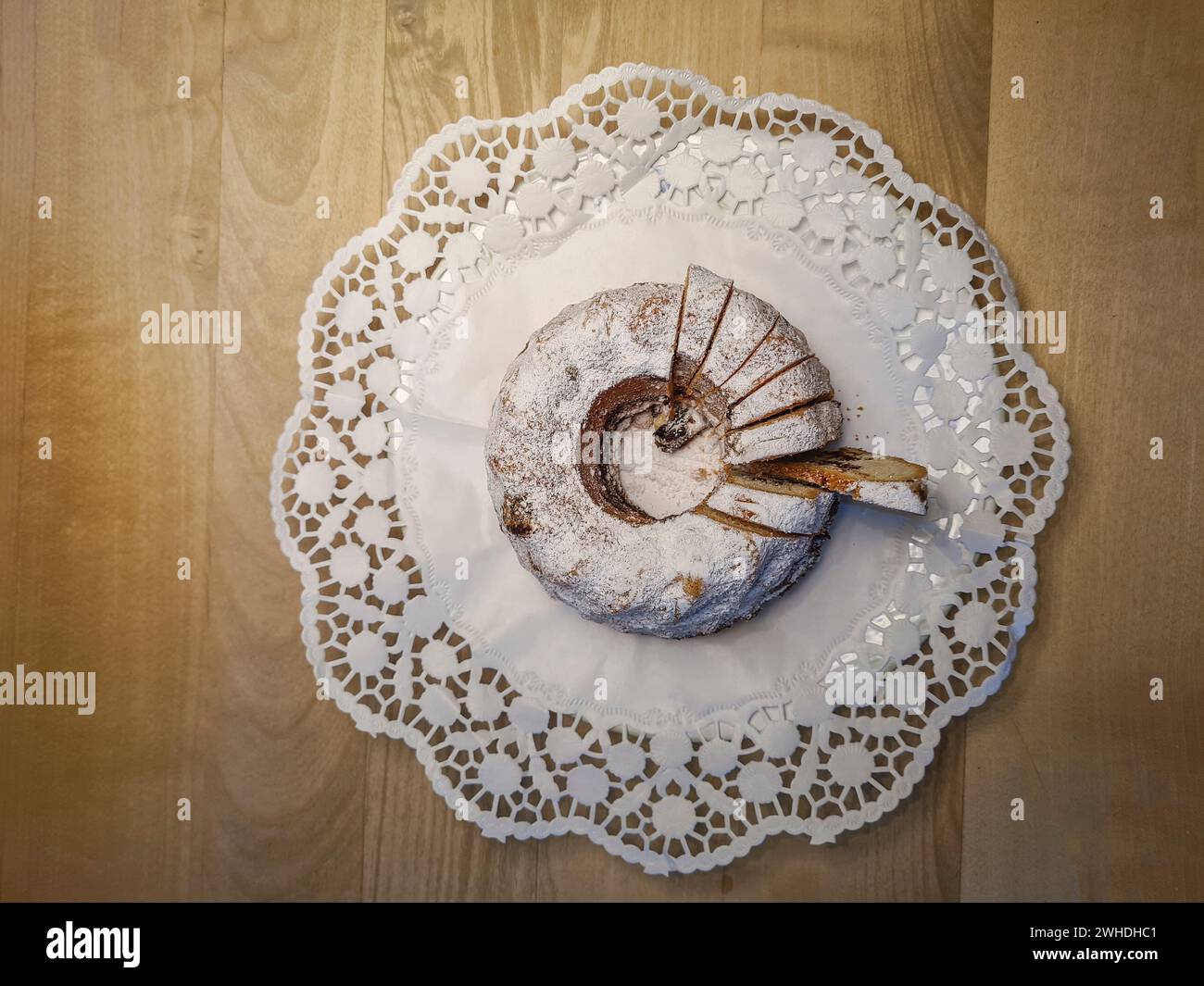 Gâteau rond en marbre avec du sucre en poudre et des miettes sur une nappe de papier blanc comme décoration sur une table en bois Banque D'Images