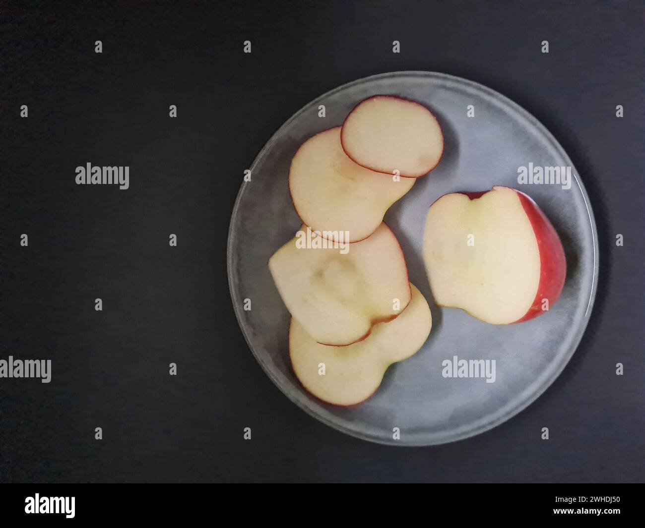 Une pomme fraîche est tranchée sur une assiette de couleur claire avec un fond sombre Banque D'Images
