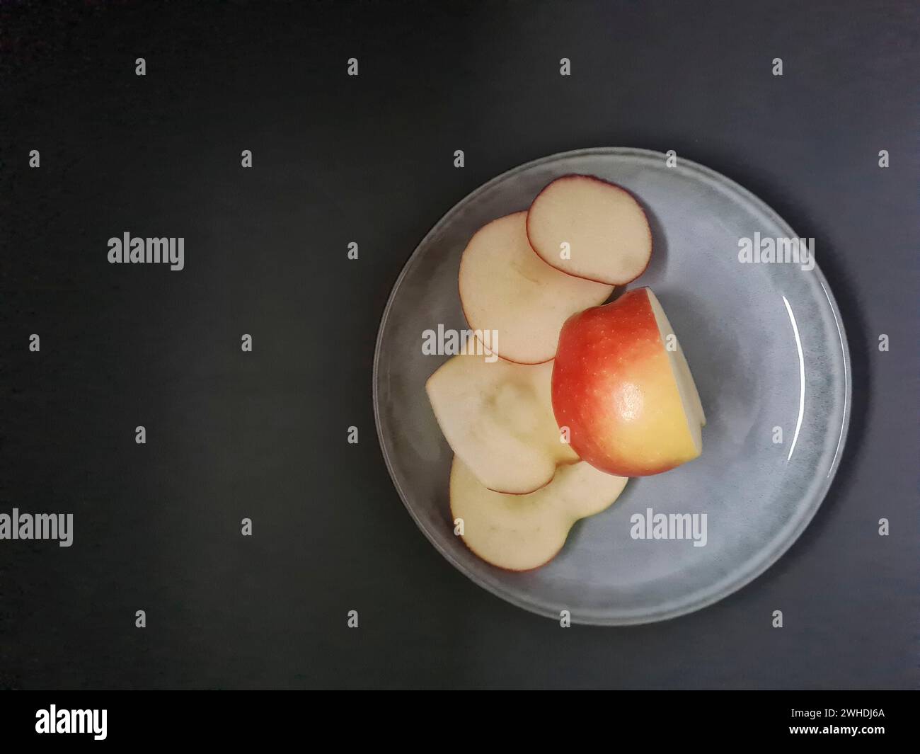 Une pomme fraîche est tranchée sur une assiette de couleur claire avec un fond sombre Banque D'Images