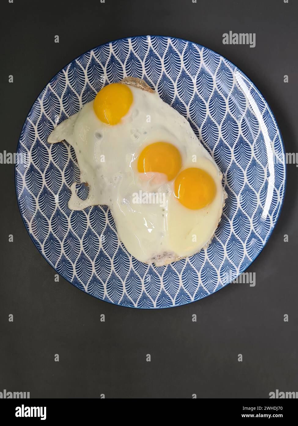 trois œufs frits sur une assiette bleue et blanche Banque D'Images