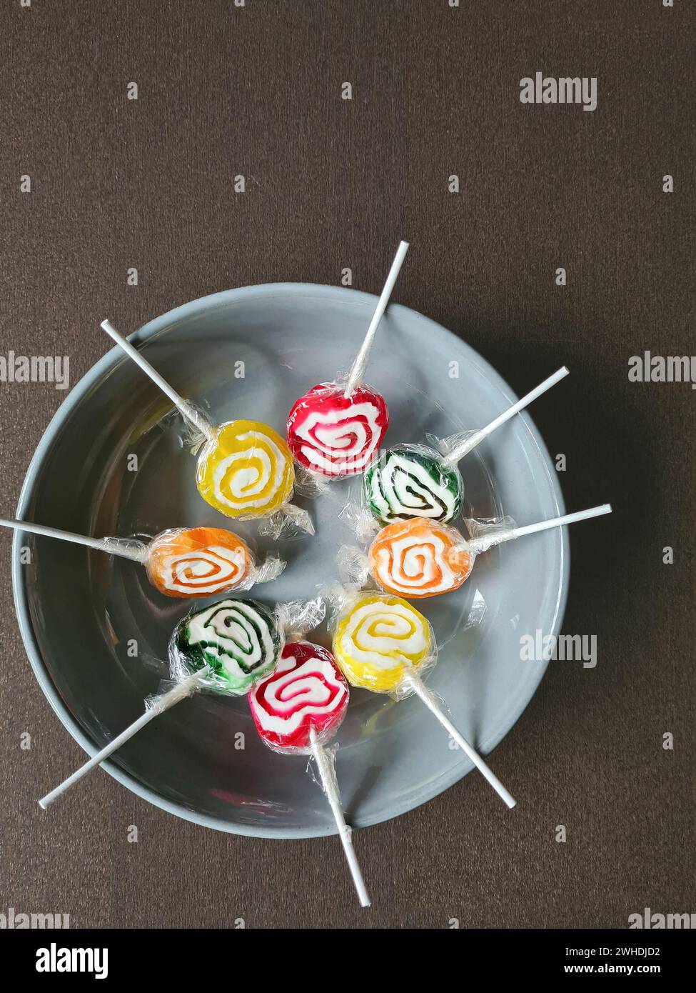 Huit sucettes sont encore enveloppées dans une feuille de plastique dans un cercle sur un bol blanc Banque D'Images