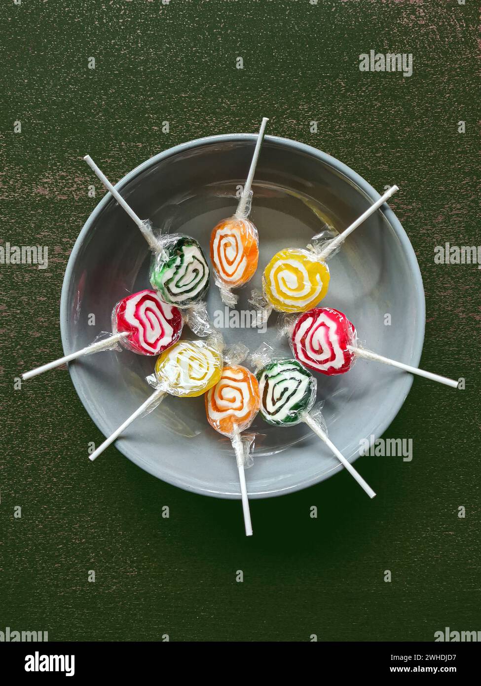 Huit sucettes colorées sont encore enveloppées dans une feuille de plastique en cercle dans un bol gris Banque D'Images