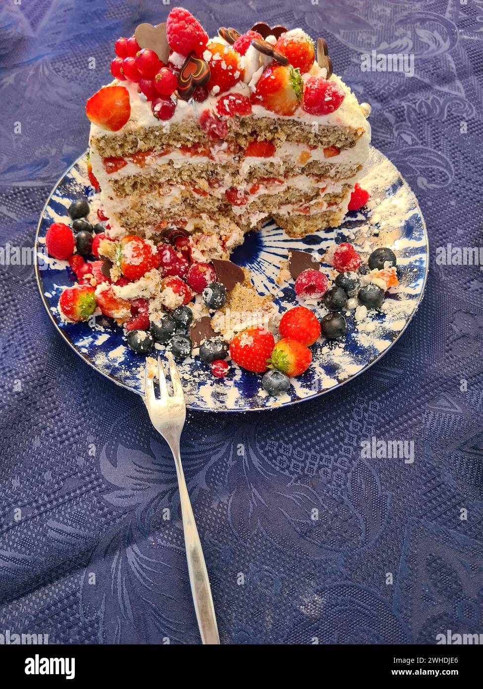 Un gâteau à la crème festif avec des fruits tels que des fraises, des framboises, des groseilles et des myrtilles comme décoration est coupé et montre la section transversale du gâteau et ses couches individuelles Banque D'Images