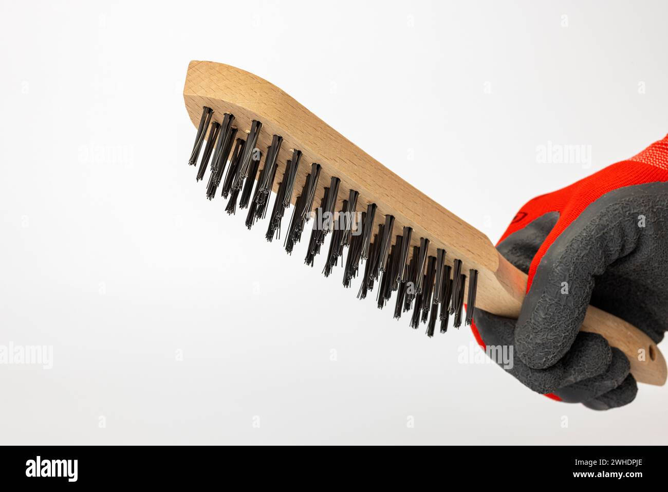 Main de l'homme avec gant de travail tenant la brosse métallique de main avec poignée en bois, brosse en acier, fond blanc, Banque D'Images