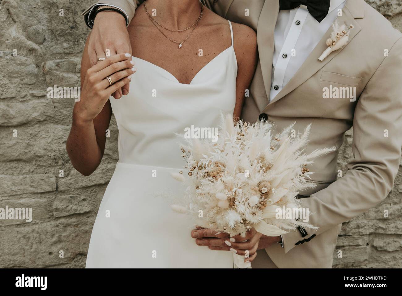 Couple marié serrant les uns les autres latéralement, se tenant les mains, bouquet de mariée de fleurs séchées en beige Banque D'Images