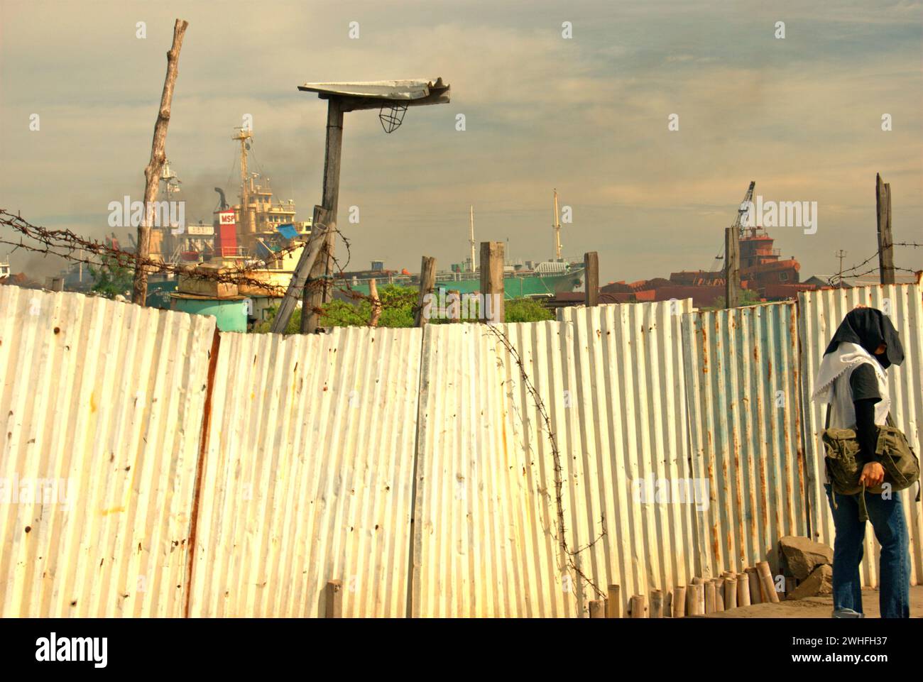 Une clôture qui sépare une route étroite avec une zone de chantier de démolition de navires, près du village côtier de Marunda à Cilincing, Jakarta, Indonésie. Banque D'Images