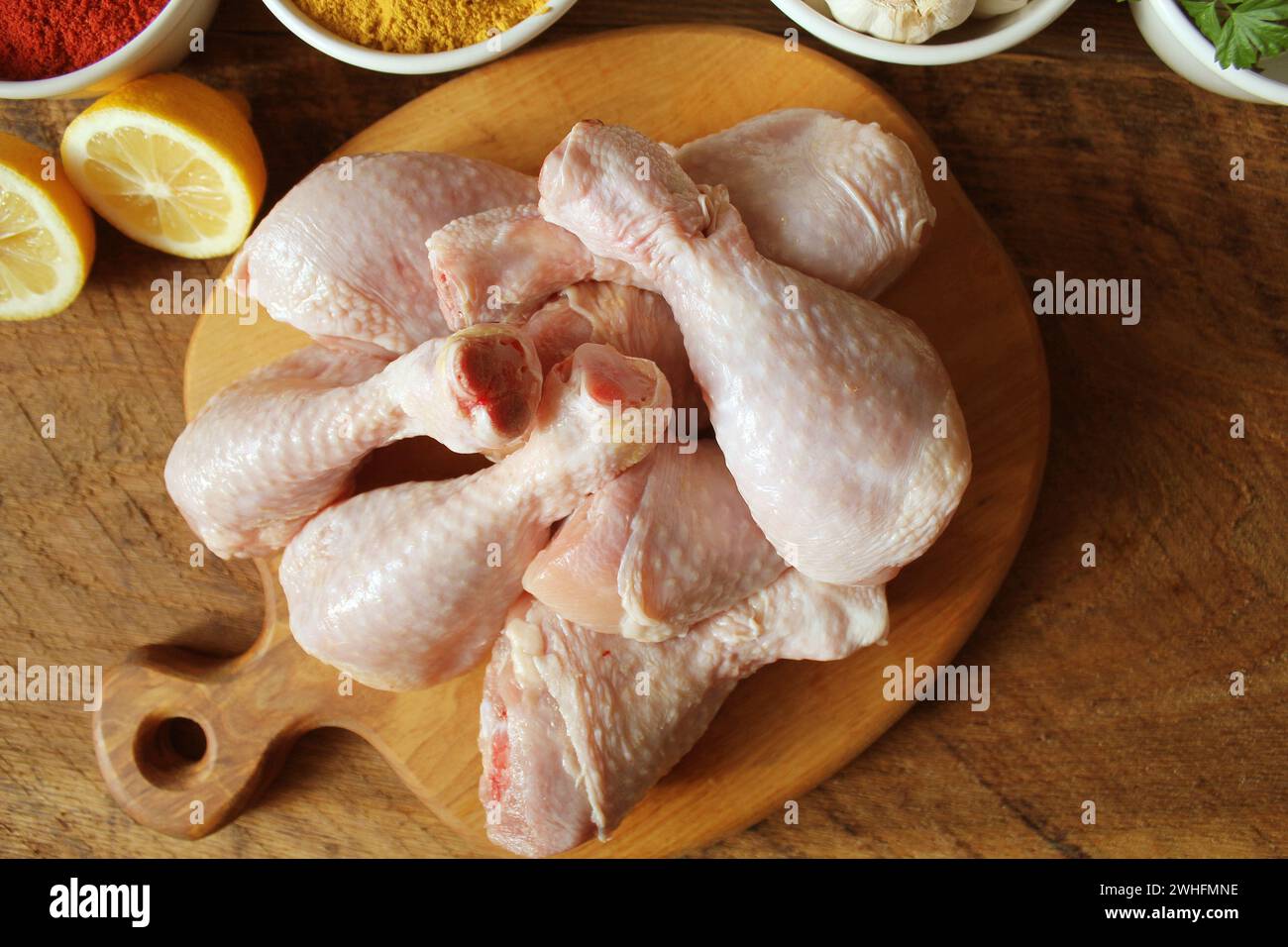Cuisses de poulet non cuit brut, les pilons sur une planche à découper, la viande avec les ingrédients pour la cuisson Banque D'Images