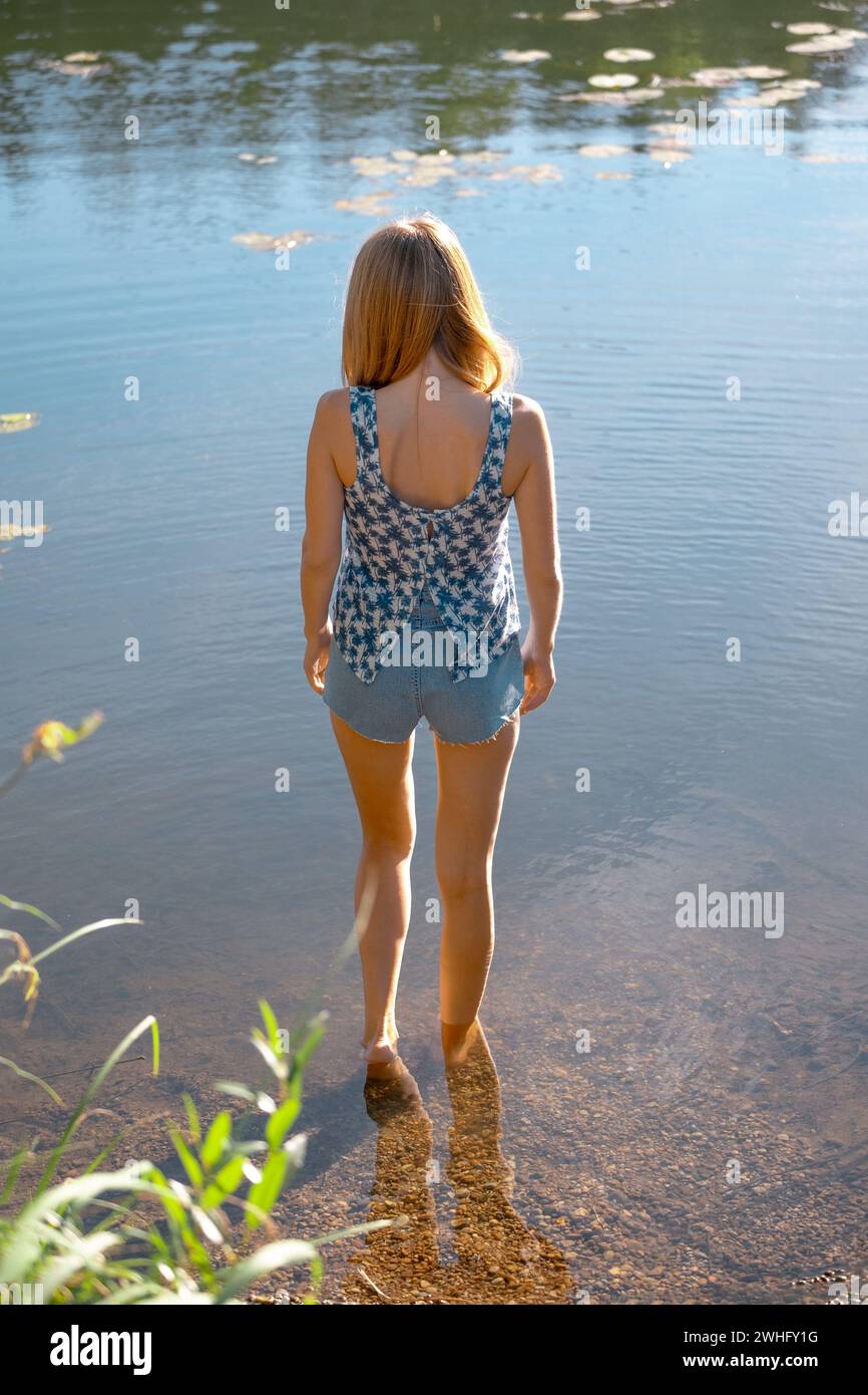 Vue arrière d'une jeune femme en chemisier et short entrant dans la rivière Banque D'Images