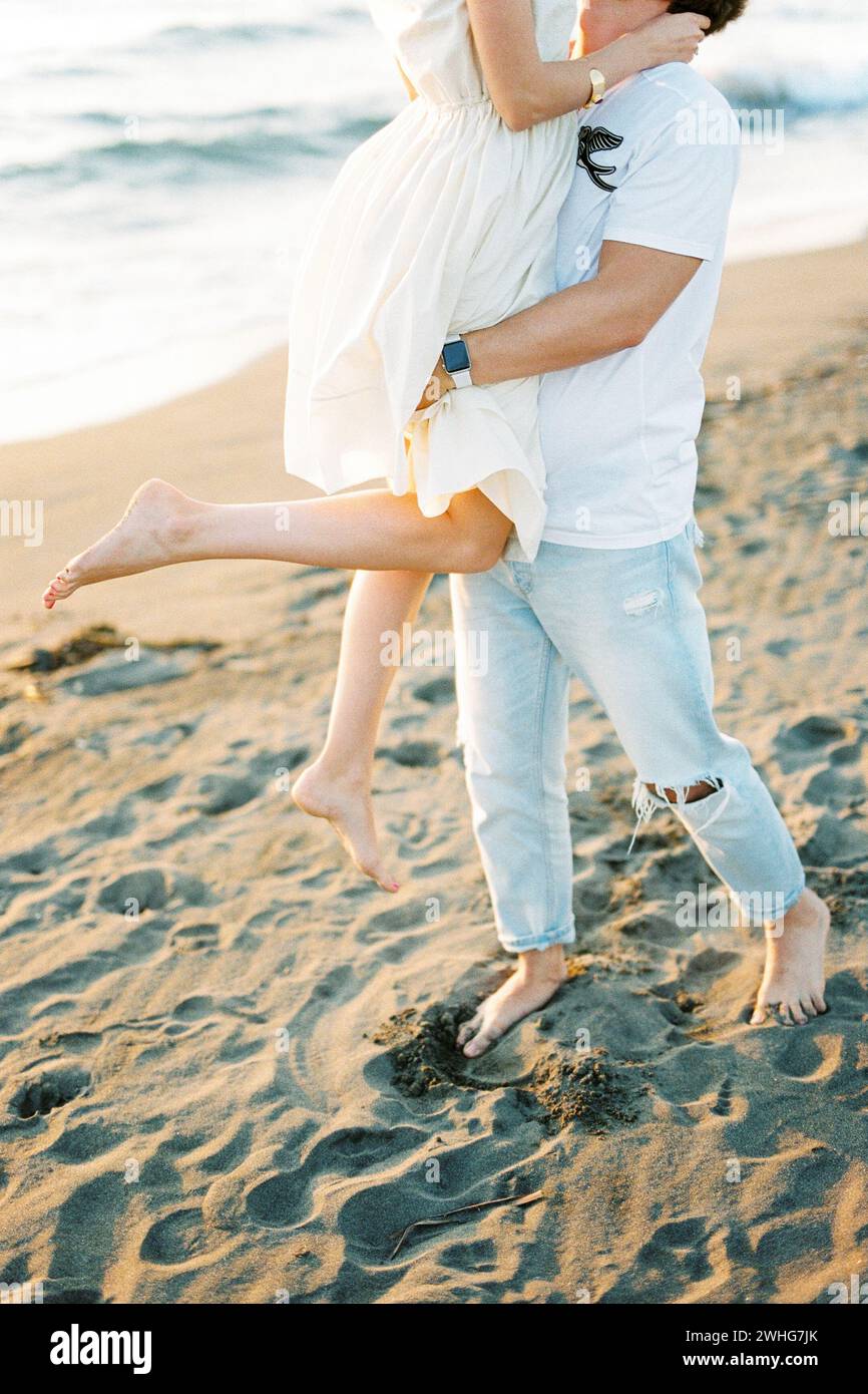 Homme tenant une femme dans ses bras sur la plage. Rogné Banque D'Images