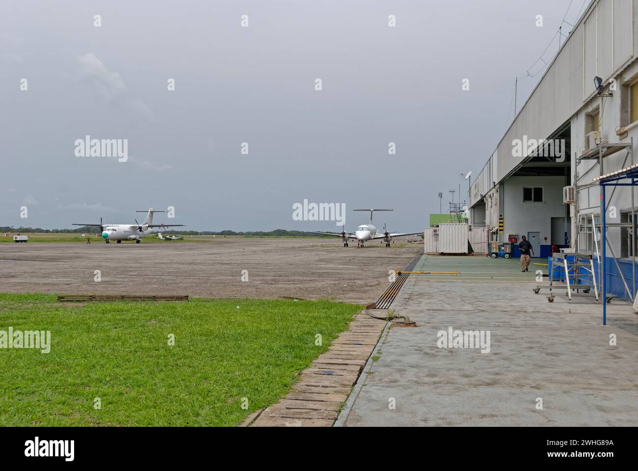 Des avions se sont garés sur l'aire de trafic de l'aéroport en béton de Port gentil un jour couvert de décembre, avec des employés de l'aéroport marchant près du terminal Bui Banque D'Images
