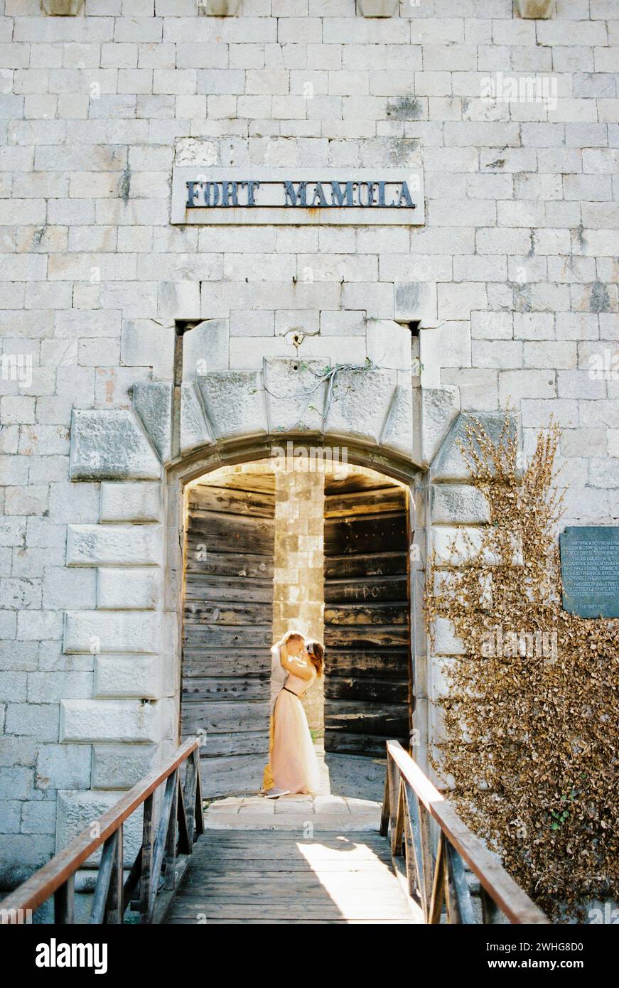 Le marié embrasse la mariée derrière la porte en bois entrouverte de Mamula Fort Banque D'Images