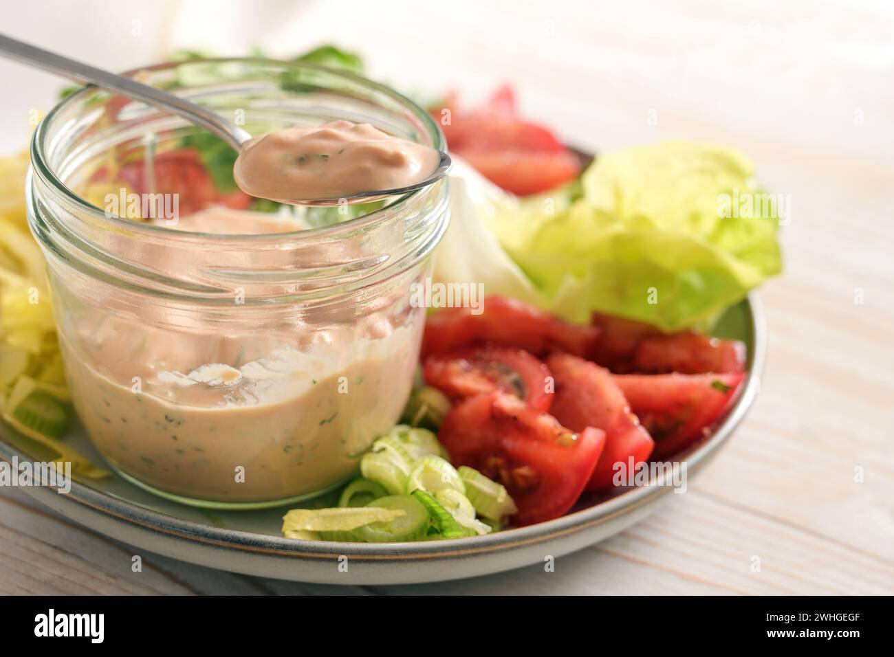 Vinaigrette à salade de skyr sur une cuillère et dans un pot en verre sur une assiette avec des tranches de laitue et de tomates, repas cru sain Banque D'Images