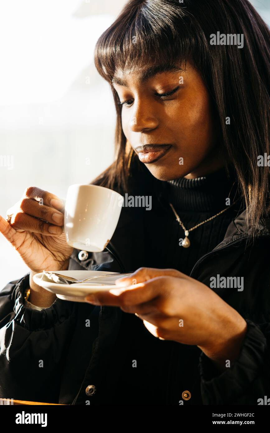 Gros plan portrait d'une jeune belle femme africaine buvant du café dans un café. Banque D'Images