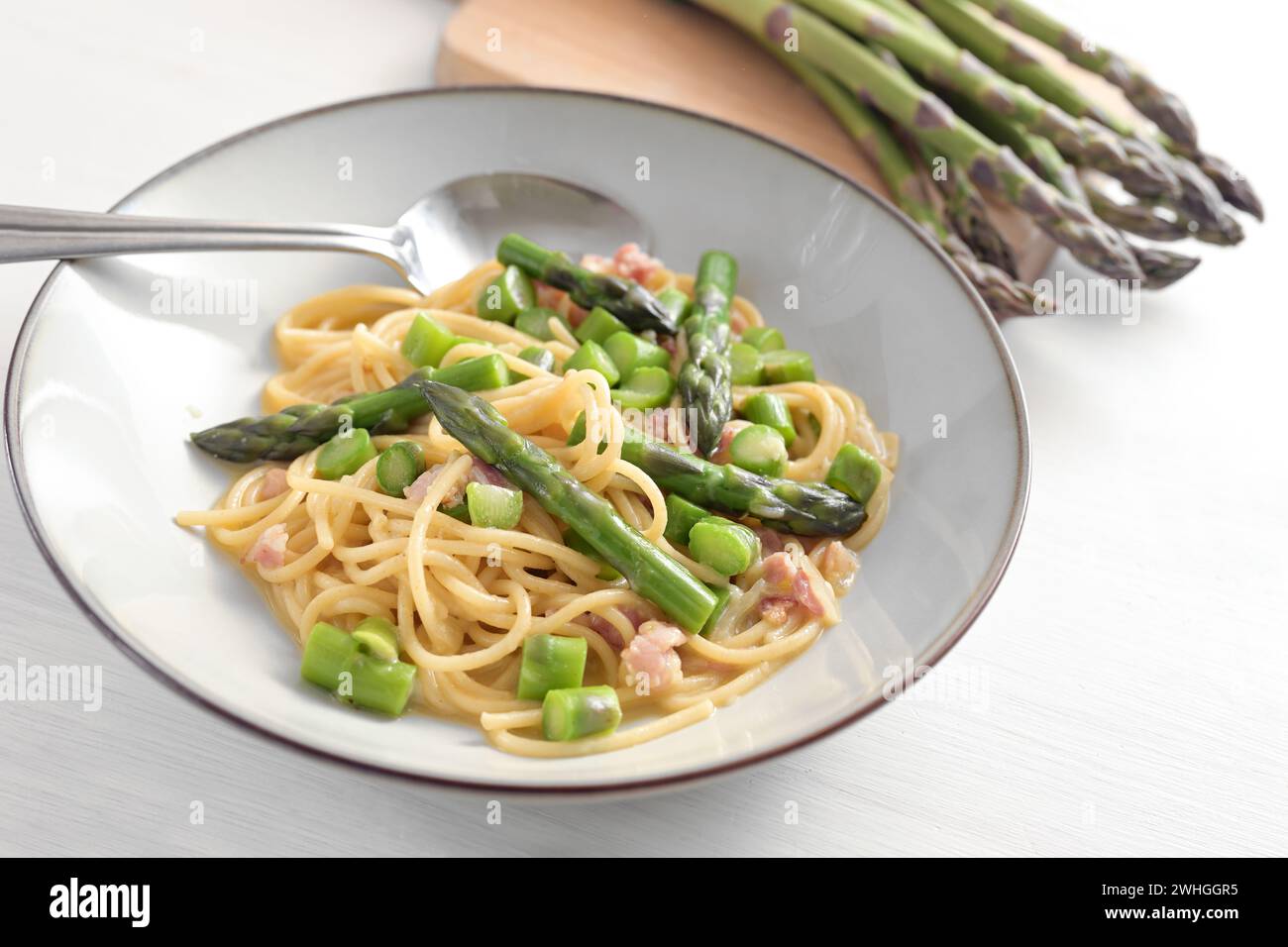 Spaghetti aux asperges vertes, bacon et oeuf comme variation de sauce carbonara sur une assiette et sur une table en bois peinte en blanc, selec Banque D'Images