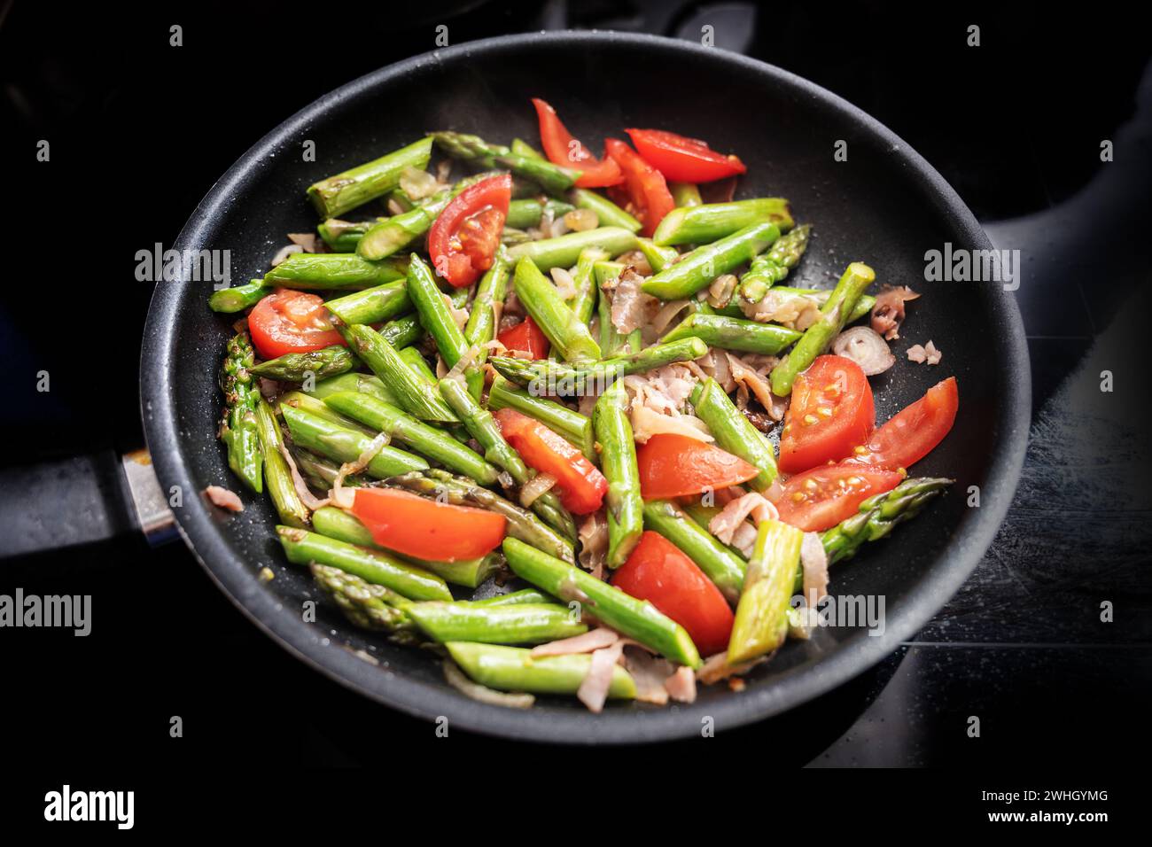 Asperges vertes, tomates et jambon de Parme dans une poêle noire sur la cuisinière, la cuisson d'un repas de printemps sain, focu sélectionné Banque D'Images