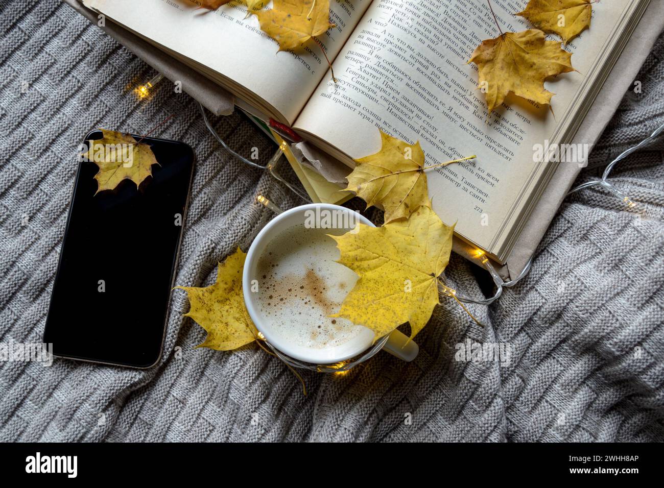Un livre, une tasse de café et un téléphone parsemé de feuilles d'érable jaunes Banque D'Images