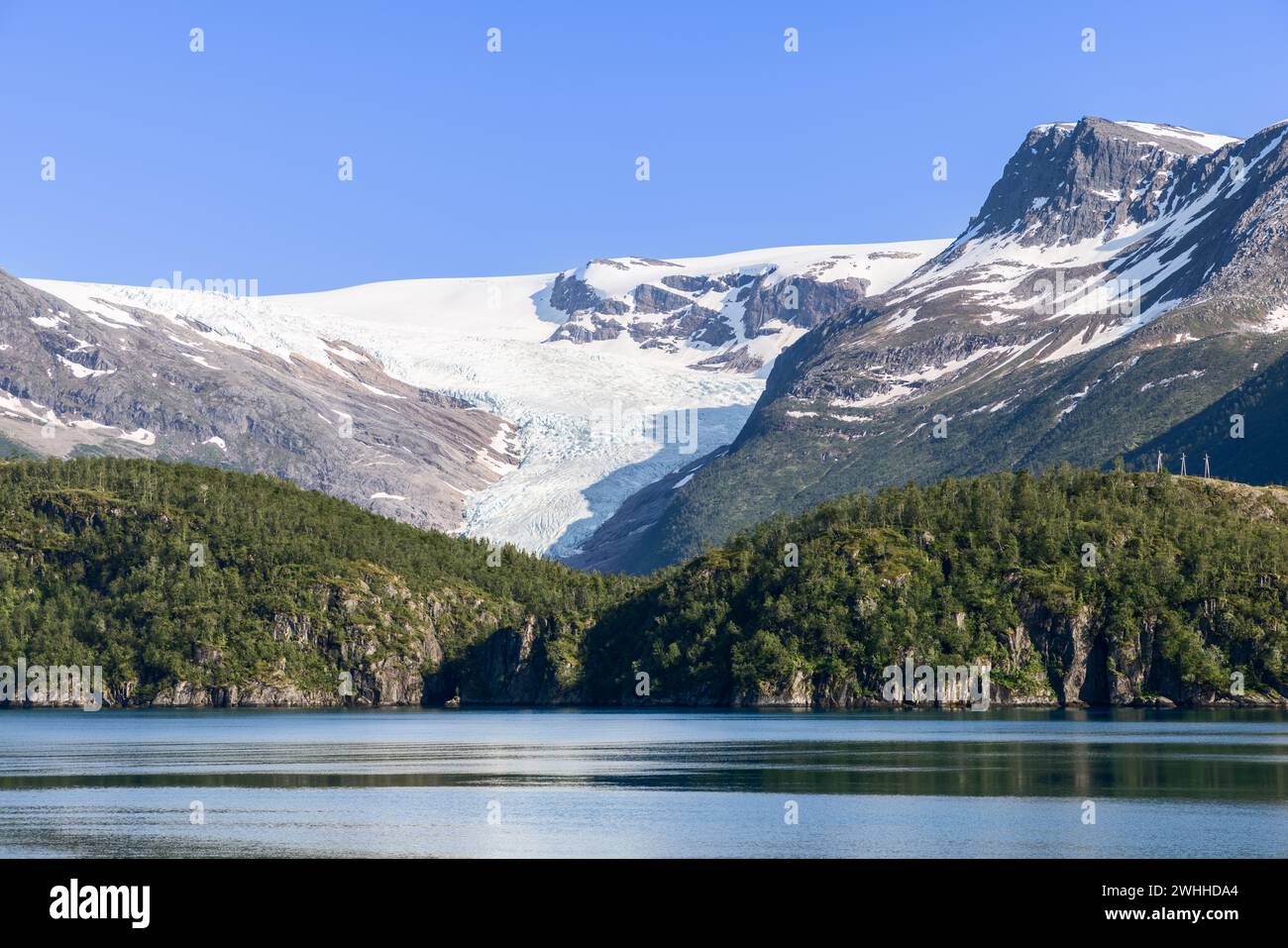 Le glacier Svartisen, drapé de blanc immaculé, se distingue des sommets accidentés, tandis que les eaux tranquilles du lac reflètent la sérénité nordique Banque D'Images