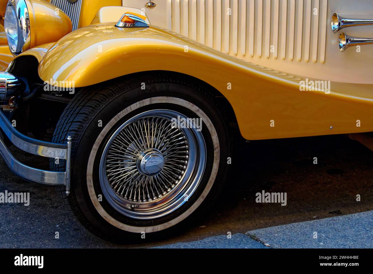 Un gros plan de la face avant d'une voiture vintage jaune, mettant en valeur la roue à rayons métalliques détaillée, le pare-chocs chromé et la conception de carrosserie élégante. Banque D'Images