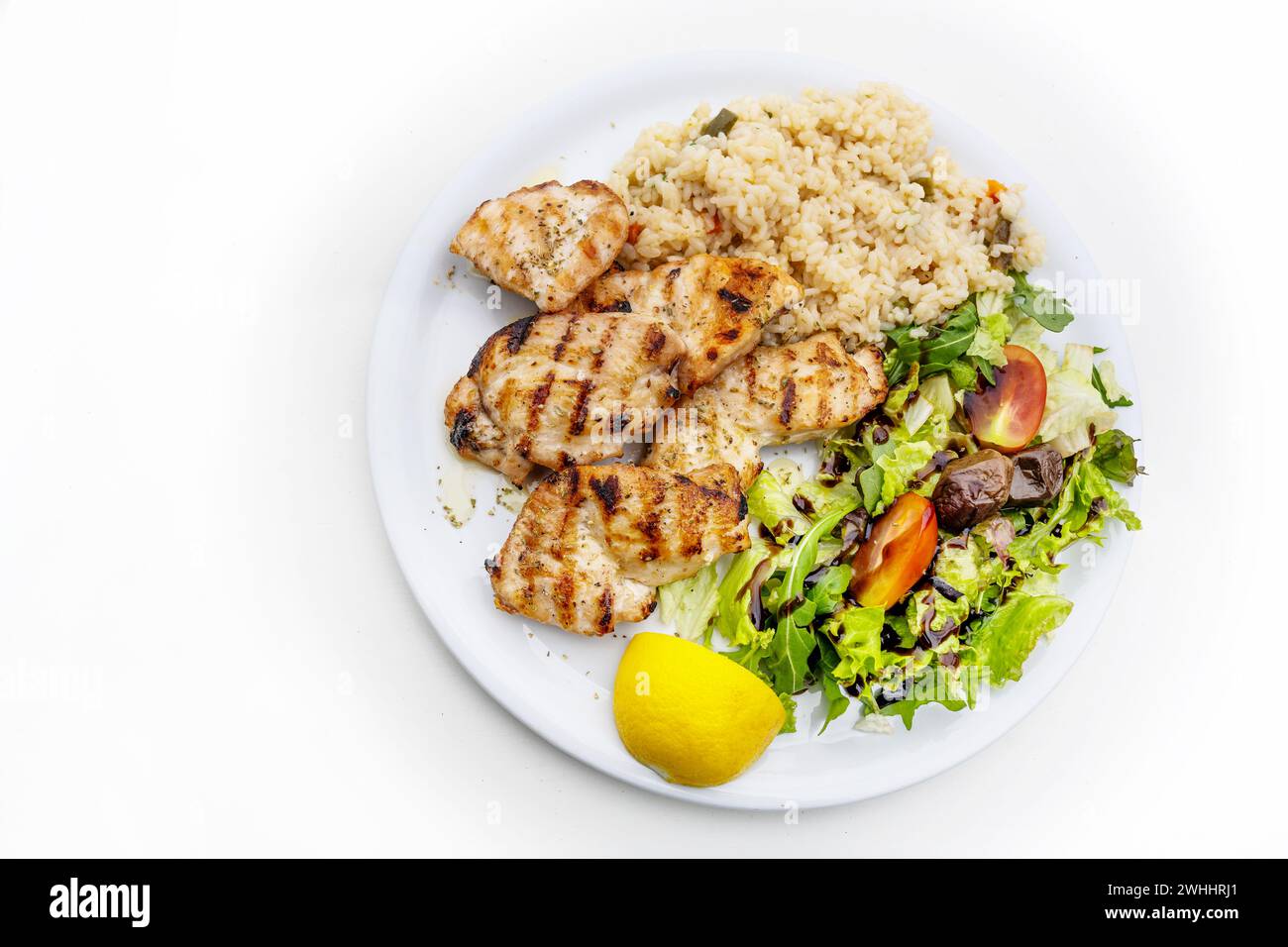 Filet de poulet grillé avec salade mixte, riz et citron, plat méditerranéen servi sur une assiette, table blanche, espace copie, haut ang Banque D'Images