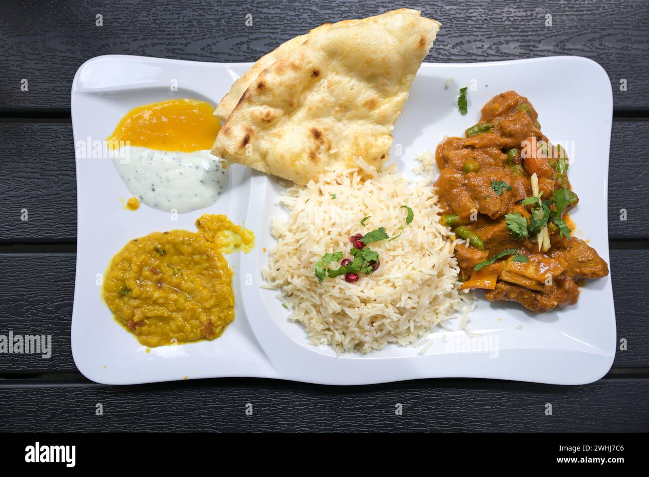 Plat indien de viande de bœuf avec sauce, riz, pain, lentilles et trempettes, servi sur une assiette blanche et une table sombre, vue en haut angle fr Banque D'Images