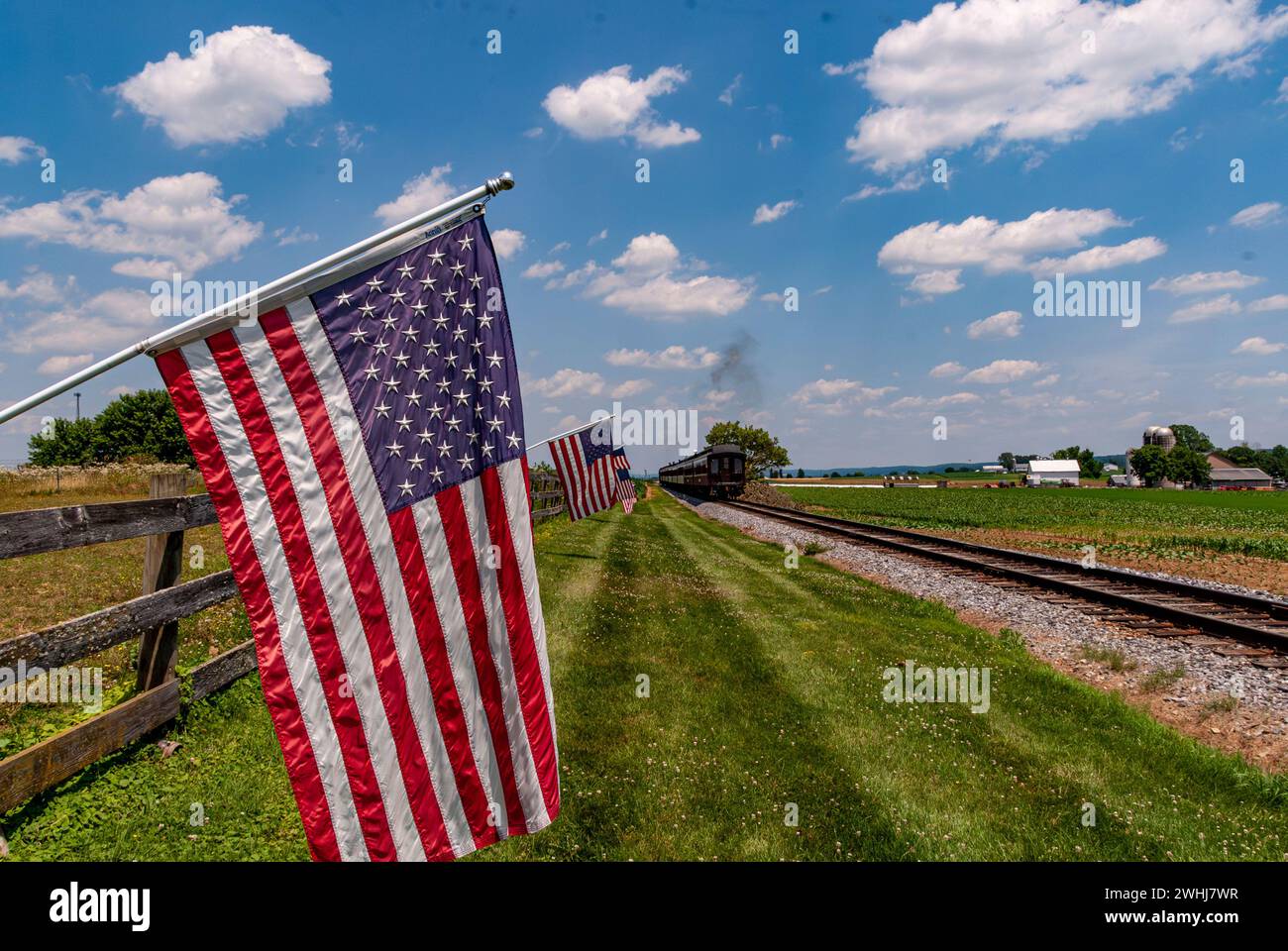 Vue des drapeaux américains agitant sur une clôture après le passage d'un train de passagers à vapeur Banque D'Images