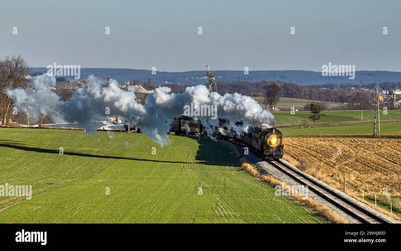 Drone vue d'un train de passagers à vapeur antique approchant voyageant à travers la campagne et les terres agricoles soufflant de la fumée Banque D'Images