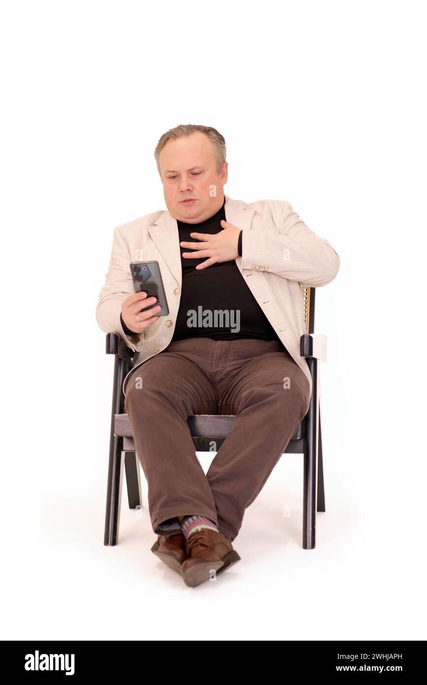 l'homme dans une chaise éprouve des émotions tout en regardant quelque chose sur son téléphone sur un fond blanc Banque D'Images