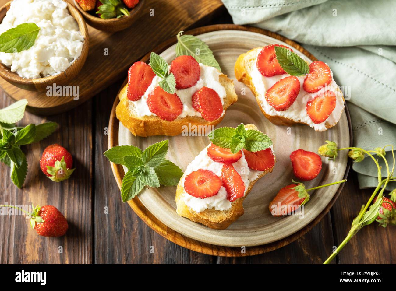 Petits pains grillés petit déjeuner, nourriture saine. Sandwich avec des fraises et du fromage à pâte molle sur fond de bois. Banque D'Images