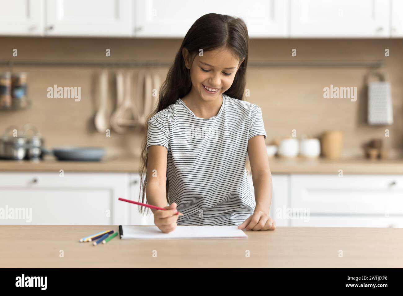 Jeune fille préadolescente positive joyeuse faisant une tâche scolaire artistique à la maison Banque D'Images