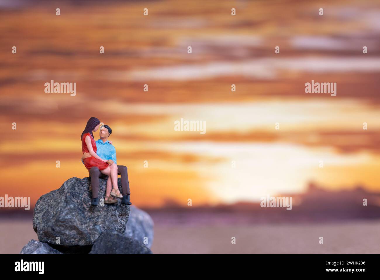 Personnages miniatures, couple assis sur une plage de mer avec fond de coucher de soleil Banque D'Images