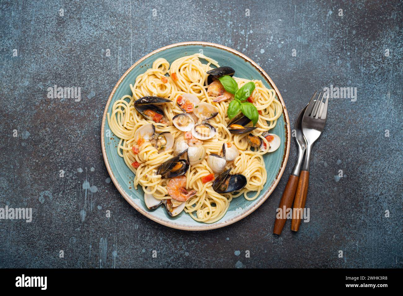 Pâtes italiennes de fruits de mer spaghettis avec moules, crevettes, palourdes en sauce tomate avec basilic vert sur assiette sur béton bleu rustique b Banque D'Images
