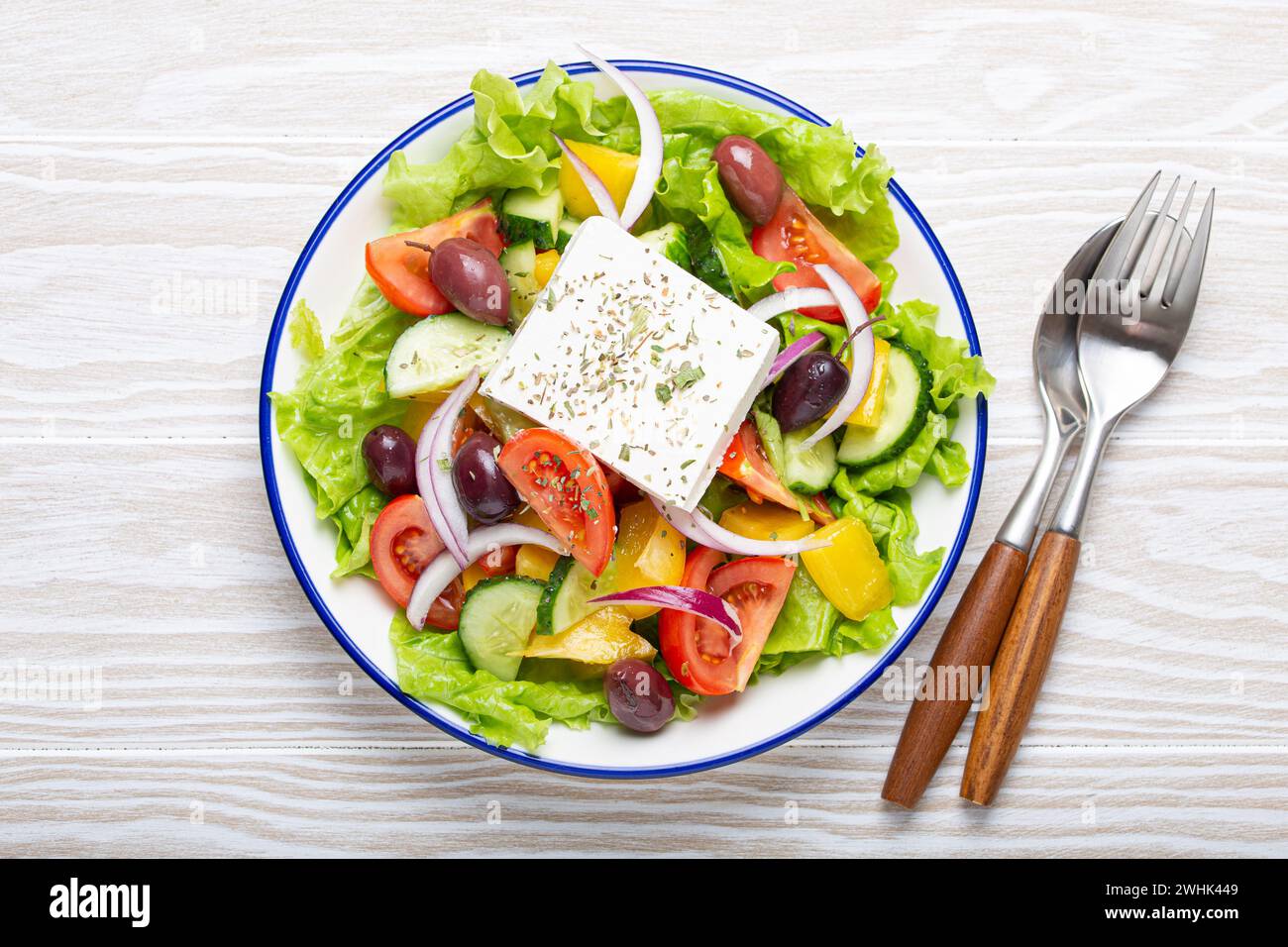 Salade grecque traditionnelle avec fromage Feta, tomates, poivron, concombres, olives, herbes dans un bol en céramique blanche sur blanc rustique Banque D'Images