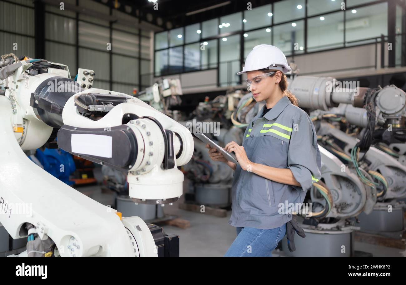 Une ingénieure installe un programme sur un bras robotique dans un entrepôt de robots. Et tester l'opération avant d'envoyer la machine t Banque D'Images