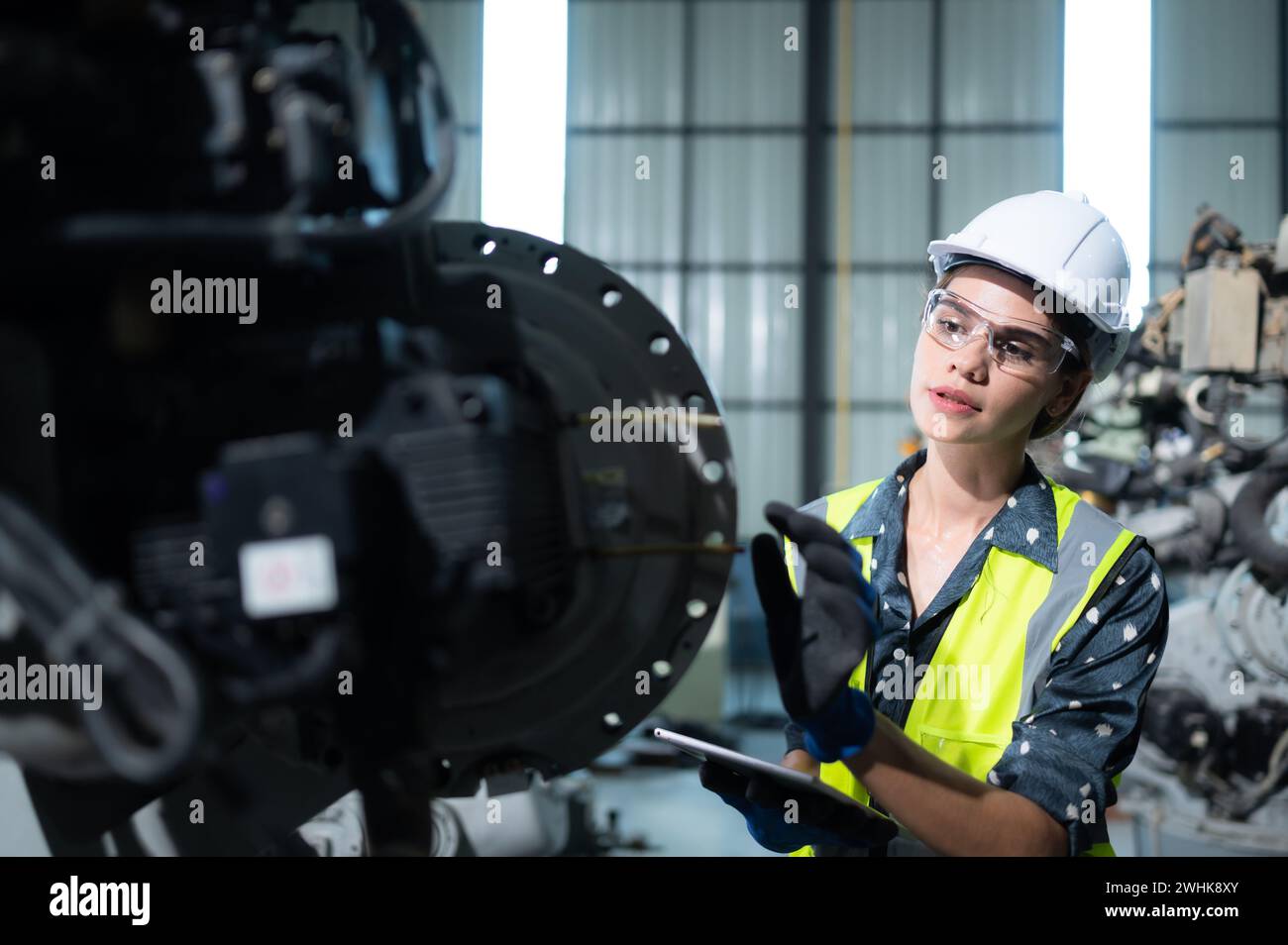 Une ingénieure installe un programme sur un bras robotique dans un entrepôt de robots. Et tester l'opération avant d'envoyer la machine t Banque D'Images