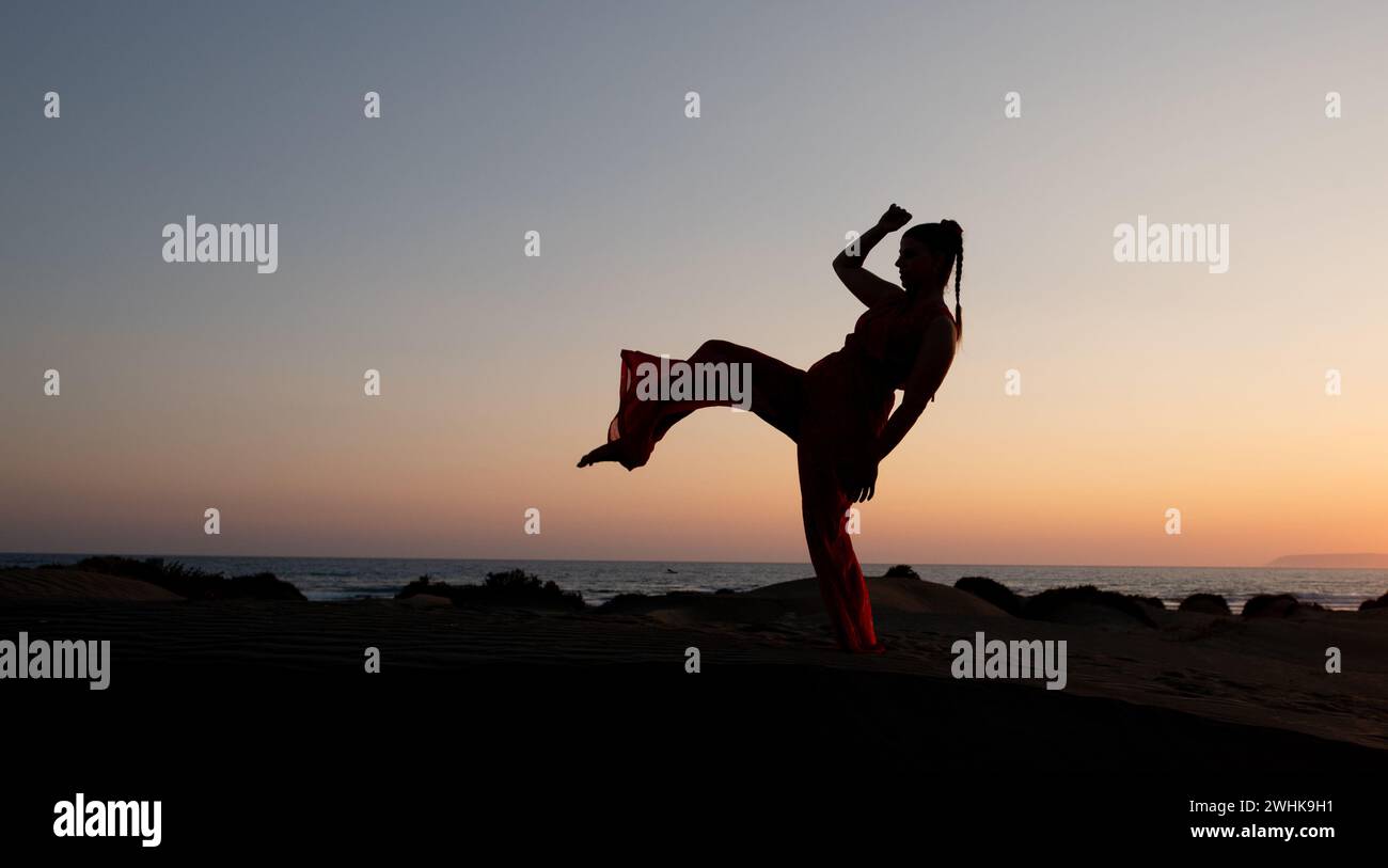 Silhouette d'une femme dansant sur une plage de sable au coucher du soleil. Femme caucasienne posant à l'extérieur sur la côte Banque D'Images