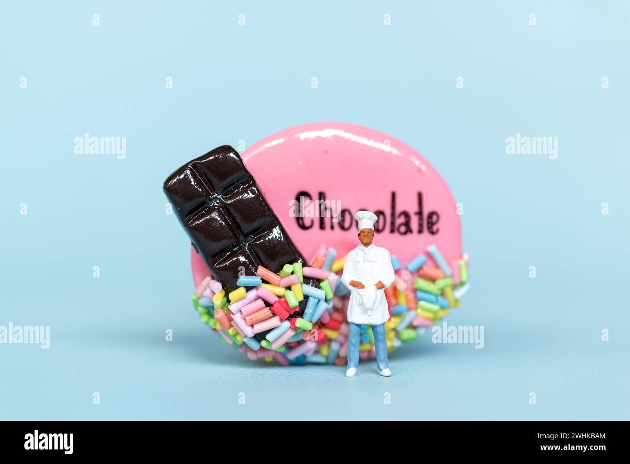 Personnes miniatures, Chef avec biscuit au chocolat sur fond bleu. Concept de la Journée mondiale du chocolat Banque D'Images