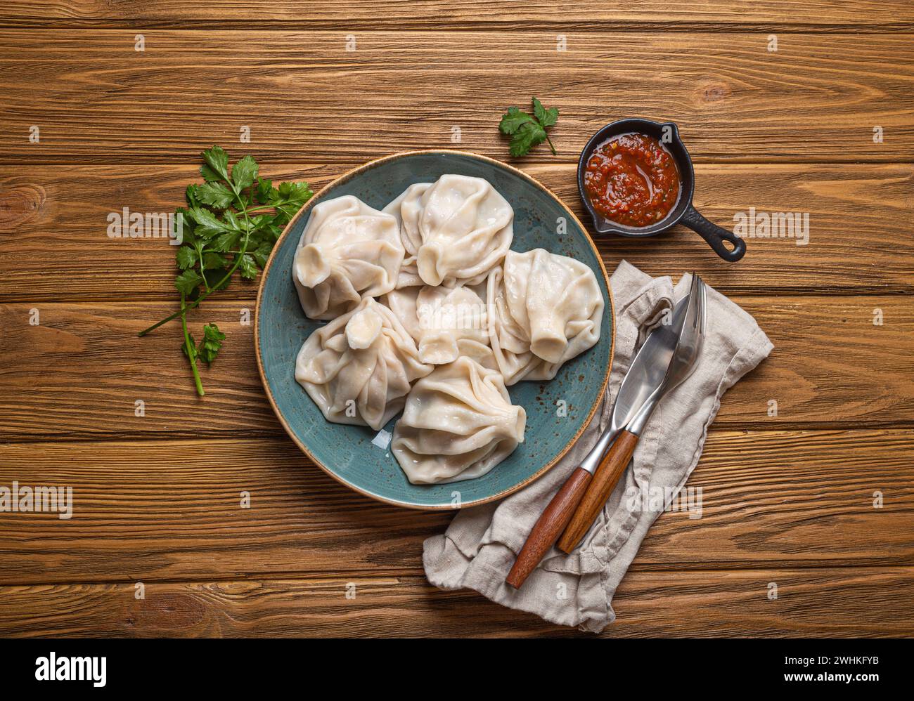 Boulettes géorgiennes Khinkali sur une assiette avec sauce tomate rouge et coriandre fraîche vue de dessus, fond de bois rustique, di traditionnel Banque D'Images