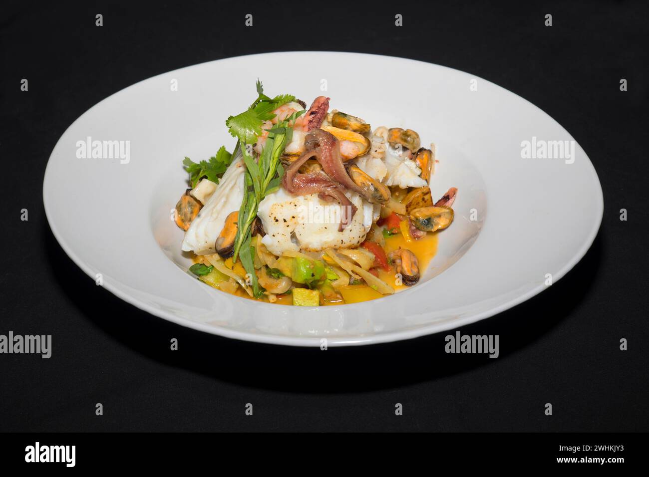 Filet de skrei norvégien rôti sur légumes colorés, avec anchois, moules, armoiries de poulpe, crevettes, coriandre fraîche et estragon, nourriture Banque D'Images