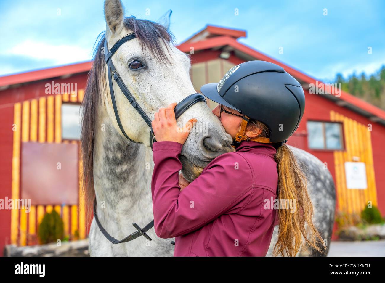 Femme avec casque de sport embrassant un cheval à l'extérieur d'un centre équestre Banque D'Images