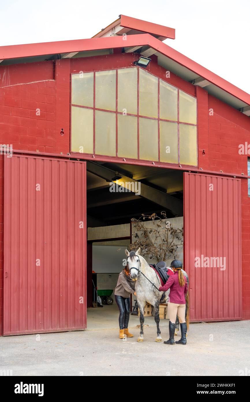 Vue large d'un bâtiment extérieur avec une jockey femme sur le point de monter un cheval dans le centre équestre Banque D'Images